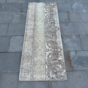 May include: A rectangular, vintage-style rug with a patchwork design. The rug features a combination of beige, cream, and brown tones, with intricate floral and geometric patterns. The rug is placed on a gray stone surface.