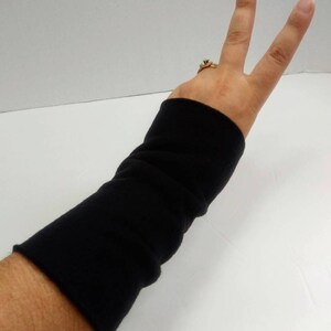 May include: Black arm warmers made of a soft, stretchy fabric. The warmers are shown on a person's arm, extending from the wrist to the elbow.