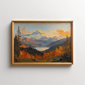 Op de afbeelding: Een ingelijst landschapsschilderij toont een bergketen bij zonsondergang. De met sneeuw bedekte top wordt verlicht door goudkleurig licht, met een meer en kleurrijke herfstbomen op de voorgrond. Het schilderij zit in een gouden lijst.