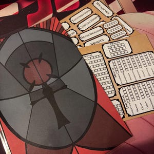 May include: A collection of tabletop role-playing game components. Includes character sheets with labeled sections for stats and skills, and cards labeled "WEAPONS", "TOUCHSTONES", "CONVICTIONS", "BACKGROUNOS", and "MERITS". The art style is reminiscent of stained glass.