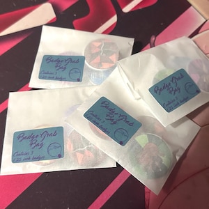Puede incluir: Varias bolsas de papel blanco pequeñas, cada una con una etiqueta que dice "Badge Grab Bag" y contiene 3 insignias. Las insignias tienen 3,18 cm de diámetro y presentan varios diseños coloridos.