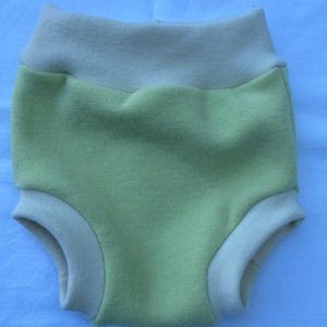 Könnte beinhalten: Eine Überhose für Windeln mit einem hellgrünen Mittelteil sowie einem kontrastierenden hellbeigen Taillenbund und Beinbündchen. Das Kleidungsstück hat eine weiche, texturierte Optik mit hohem Bund und elastischen Öffnungen an Taille und Beinen.