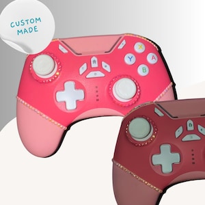 May include: Two custom-made pink and red Xbox controllers with white buttons and a crystal-like design. The text "LAX AND LUSH" and "CUSTOM MADE" are visible on the image. The text "XBOX CONTROLLER" is also visible.