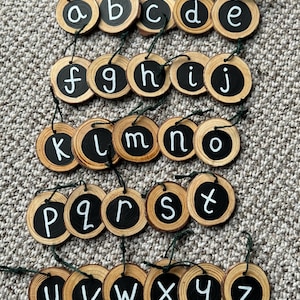 May include: A set of 26 wooden alphabet letter decorations, each with a black background and white letter painted on it. The letters are strung together with green twine.