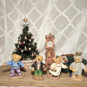 May include: A collection of four miniature teddy bear figurines, a small Christmas tree with a star topper, and a tall grandfather clock. One bear wears a blue jacket, one has an eye patch, one wears a white dress, and one wears a crown.