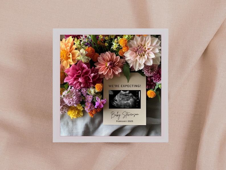 May include: A white card with the text "We're Expecting!" and a black and white ultrasound image. The card also says "Baby Stevenson" and "February 2023". The card is surrounded by a bouquet of pink, yellow, and orange flowers.