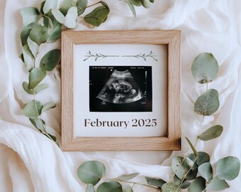 May include: A wooden frame with a white background and a black and white ultrasound image inside. The frame has a simple floral design and the text "February 2025" printed below the image.