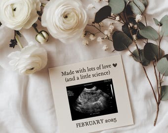 May include: A pregnancy announcement card with the text "Made with lots of love (and a little science)" and "FEBRUARY 2025". The card features an ultrasound image and is surrounded by white flowers and greenery on a white fabric background.