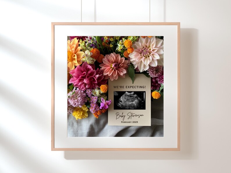 May include: A framed print featuring a floral arrangement of pink, orange, and yellow flowers. A card with the text "We're Expecting!" and an ultrasound image is placed on top of the flowers. The card also includes the text "Baby Stevenson, February 2023."