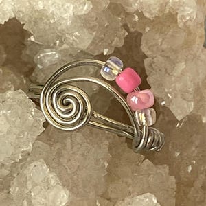 May include: A silver wire ring with a spiral design and pink and clear beads.