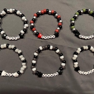 Può includere: Sei braccialetti di perline colorate con ciondoli a forma di stella e nomi scritti in perline nere. I nomi sono "Starr", "Bucky", "Belova", "Ava", "Barnes" e "Yelena".