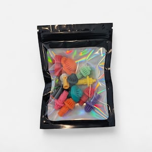May include: A black, resealable bag with a clear, iridescent interior containing an assortment of colorful, plastic components. The components are various shapes and colors, including red, orange, green, and yellow.