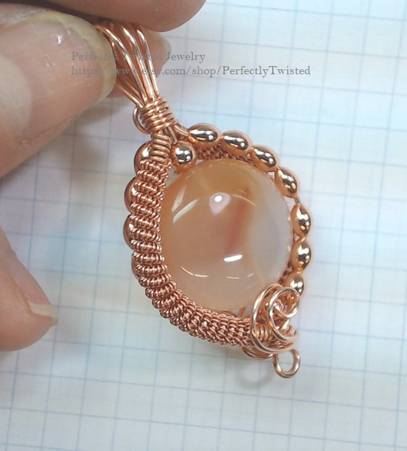 May include: A copper wire wrapped pendant featuring a round, light peach agate gemstone. The pendant has a copper wire loop for attaching to a chain or cord.