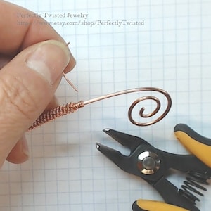 May include: A close-up of a copper wire being bent into a spiral shape using a pair of pliers. The wire is being held in place by a hand.