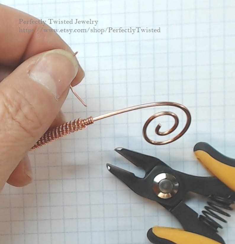 May include: A close-up of a copper wire being bent into a spiral shape using a pair of pliers. The wire is being held in place by a hand.
