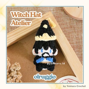 May include: A small, handmade crochet doll featuring a black witch hat with a yellow band and tassel, black hair, blue eyes, and a black outfit with blue accents. The text "Witch Hat Atelier" and "olruggio" are visible in the image.