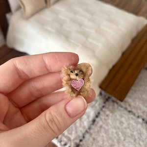 Op de afbeelding: Een kleine bruine teddybeer die een roze hart vasthoudt. De beer is gemaakt van zacht, pluche materiaal en heeft een lieve uitdrukking.