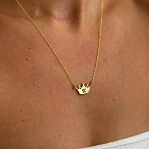 May include: A gold chain necklace with a small crown pendant featuring the letter "K" in the center.