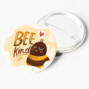 May include: A yellow and brown bee with a heart above its head and the text "BEE kind" on a yellow background with white clouds. The bee is on a round button.