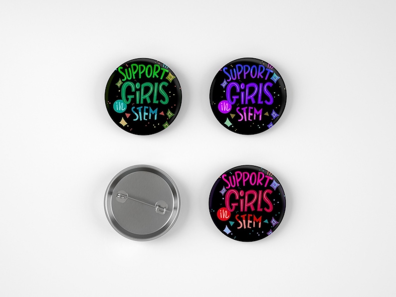 May include: Four round buttons with a black background and colorful text that reads "Support Girls in STEM". The buttons have a silver backing.