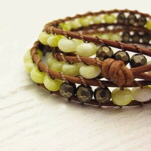 May include: A multi-strand leather wrap bracelet with green and brown beads. The bracelet is made with brown leather cord and features a knot closure.