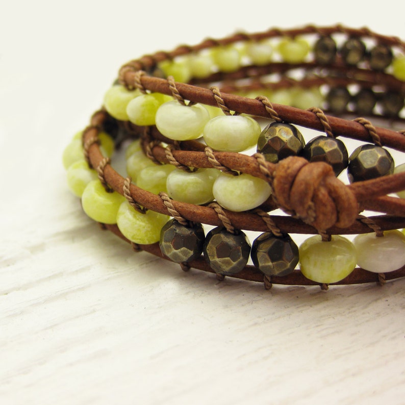 May include: A multi-strand leather wrap bracelet with green and brown beads. The bracelet is made with brown leather cord and features a knot closure.