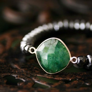 May include: A green gemstone bracelet with a large, faceted emerald-cut stone set in silver. The bracelet is made with black and silver beads.