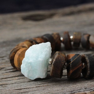 May include: A bracelet made of brown and black wooden beads with a light blue gemstone.