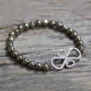May include: A silver bracelet with a large, sparkly, infinity symbol charm. The bracelet is made of small, round, dark gray beads.