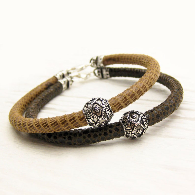 May include: Two leather bracelets with silver tone decorative beads. One bracelet is brown and the other is black.
