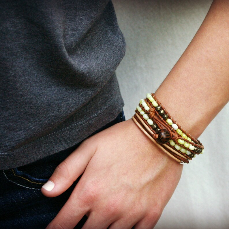 May include: A multi-layered bracelet with brown leather cord, light green and brown beads, and a brown wooden bead accent.