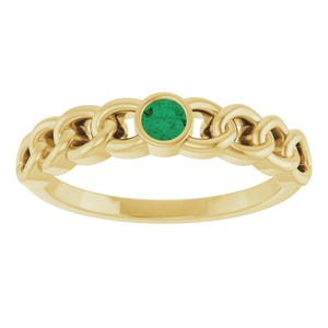 May include: A gold ring with a chain-link design. The ring has a round, emerald-green gemstone in the centre. The band is made of polished gold. A piece of jewellery.
