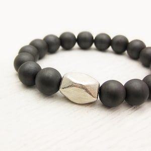 Könnte beinhalten: Ein schwarzes Perlenarmband mit einem silbernen, facettierten Perlen in der Mitte.