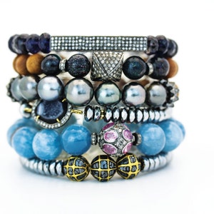 May include: A stack of bracelets with various colored beads, including blue, brown, gray, and black. Some beads are accented with small diamonds and pink stones.
