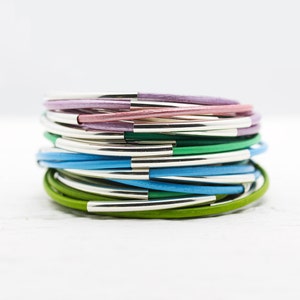 May include: A stack of colorful leather bracelets with silver accents. The bracelets are in shades of green, blue, and purple.