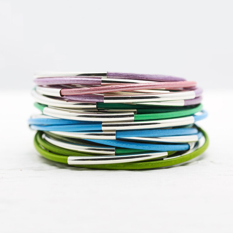 May include: A stack of colorful leather bracelets with silver accents. The bracelets are in shades of green, blue, and purple.