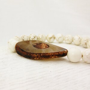 May include: A white stone bracelet with a brown and white teardrop-shaped pendant.