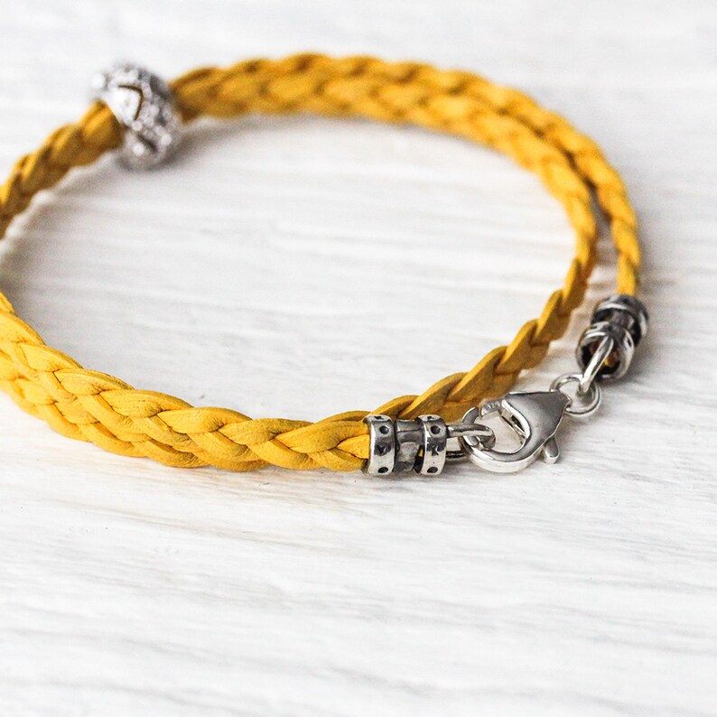 May include: A yellow braided leather bracelet with a silver clasp and a silver charm.