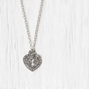 May include: A silver necklace with a heart-shaped pendant. The pendant is covered in small, clear stones and has a keyhole design in the center.