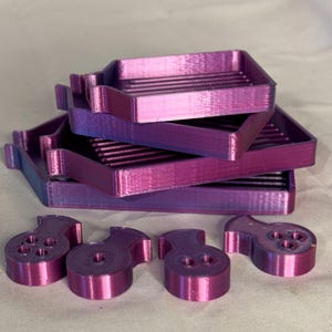 May include: Four purple 3D printed trays stacked on top of each other. Four purple 3D printed pieces with holes are in the foreground.