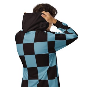 Puede incluir: Una sudadera con capucha de color negro y azul claro a cuadros. La capucha est&aacute; puesta sobre la cabeza de la persona que la lleva.