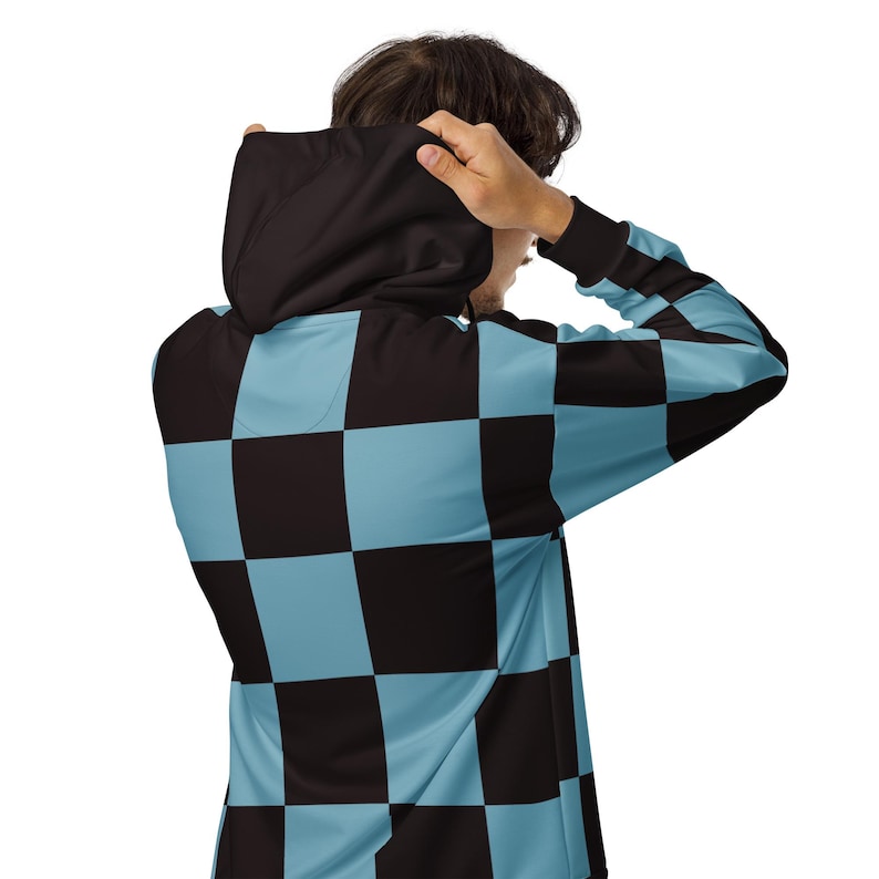 Puede incluir: Una sudadera con capucha de color negro y azul claro a cuadros. La capucha est&aacute; puesta sobre la cabeza de la persona que la lleva.