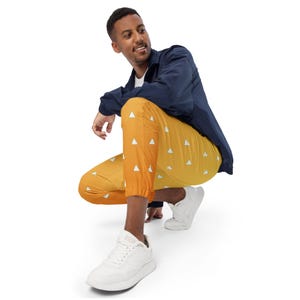 May include: Yellow and orange joggers with a white triangle pattern. The joggers have a drawstring waist and elastic cuffs. The person in the image is wearing a navy blue jacket and white sneakers.