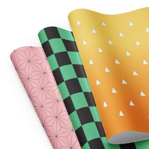 Pode incluir: Três rolos de papel estampado. Um rolo é rosa com um padrão geométrico de estrelas, outro é verde e preto xadrez, e o terceiro é amarelo e laranja com triângulos brancos. Os rolos estão parcialmente desenrolados, revelando os padrões.