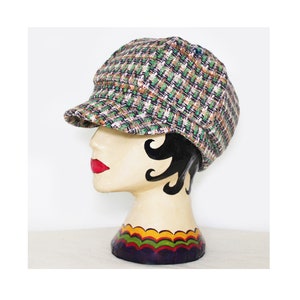 May include: A green, brown and white patterned newsboy cap with a slightly curved brim. The cap is on a mannequin head.