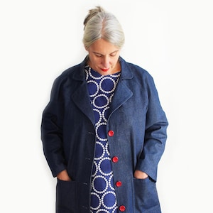May include: A woman wearing a blue denim jacket with red buttons over a blue and white patterned dress.