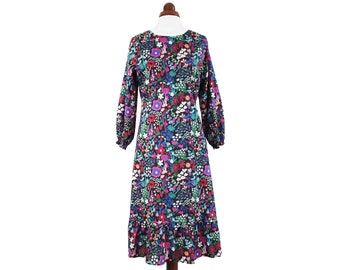 Peut inclure: Une robe midi à manches longues avec un imprimé floral dans des tons de rose, rouge, bleu, vert et blanc sur fond noir. La robe a un col rond et un ourlet à volants.