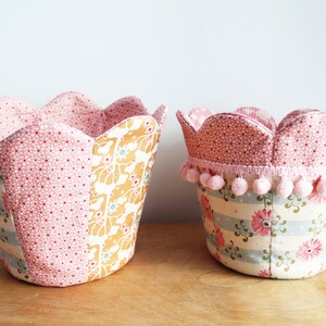 Peut inclure: Deux paniers de rangement en tissu avec des bords festonn&eacute;s. Le plus grand panier est rose avec des pois blancs et un motif floral. Le plus petit panier est rose avec des pois blancs et un motif ray&eacute; avec des fleurs roses. Les deux paniers ont une bordure en pompons roses.