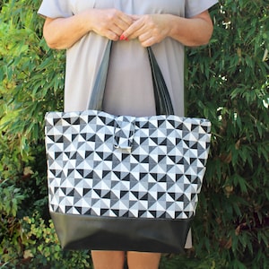 May include: A black and white geometric patterned tote bag with a black leather base. The bag has two black handles.