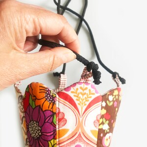 Peut inclure: Une pochette en tissu color&eacute; avec une fermeture &agrave; cordon noir. La pochette est faite de tissu patchwork avec un motif floral.